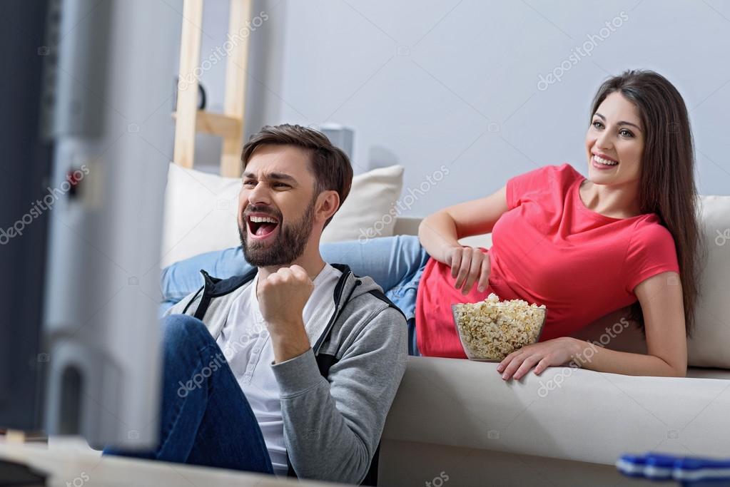 Vista traseira dos homens assistindo a um jogo de futebol na tv e sentado  em um sofá