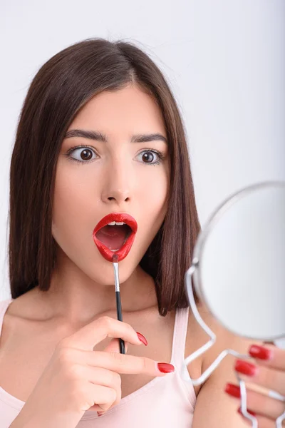 Mujer conmocionada aplicando lápiz labial rojo —  Fotos de Stock