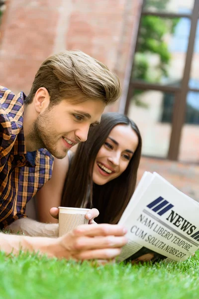 Amigos felices leyendo el periódico en el césped — Foto de Stock