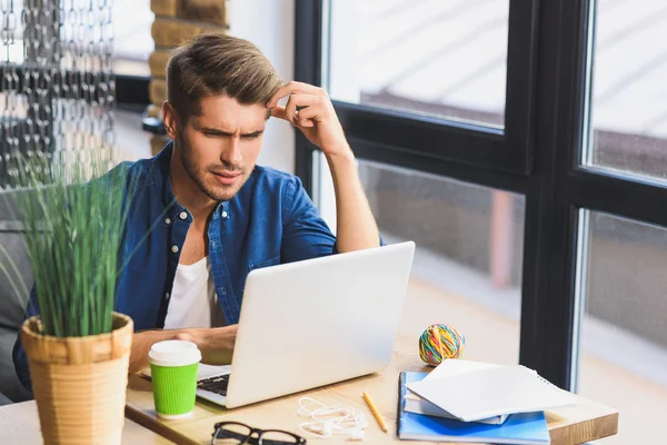 Confundido joven freelancer delante de un ordenador portátil — Foto de Stock