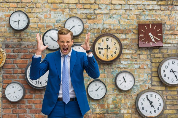 Hombre de traje de pie cerca de la pared con relojes — Foto de Stock