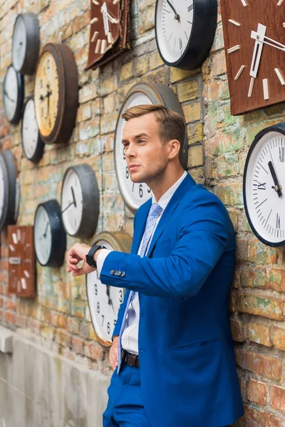Hombre de traje de pie cerca de la pared con relojes — Foto de Stock