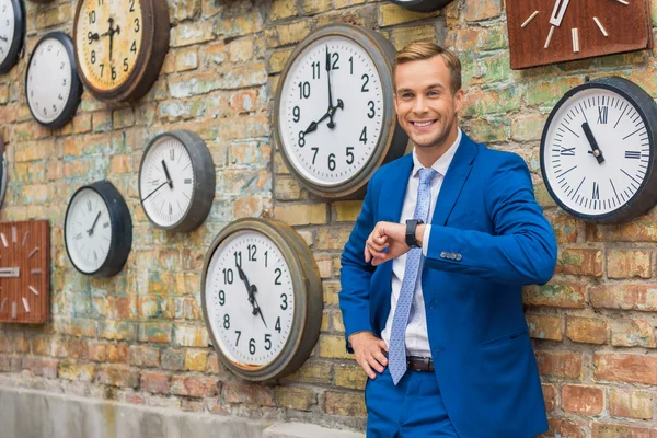 Hombre de traje de pie cerca de la pared con relojes —  Fotos de Stock