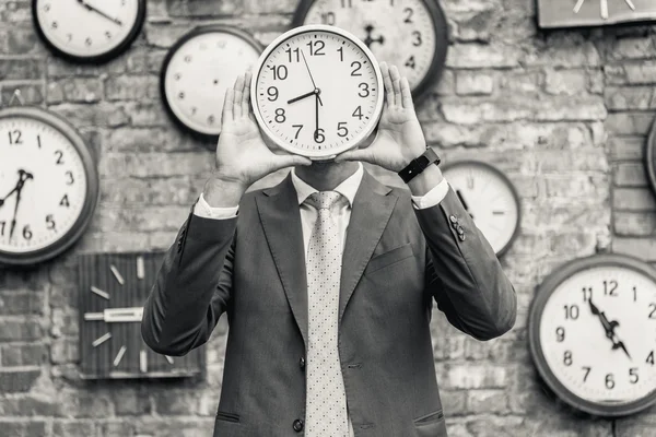 Man in suit standing near wall with clocks — Stock Photo, Image