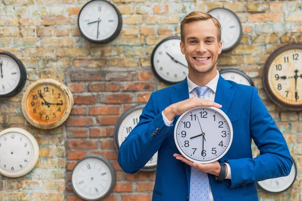 Hombre de traje de pie cerca de la pared con relojes — Foto de Stock