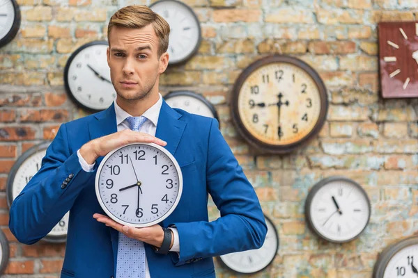 Hombre de traje de pie cerca de la pared con relojes — Foto de Stock