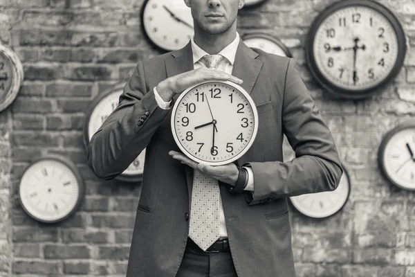 Hombre de traje de pie cerca de la pared con relojes — Foto de Stock