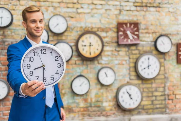 Hombre de traje de pie cerca de la pared con relojes — Foto de Stock