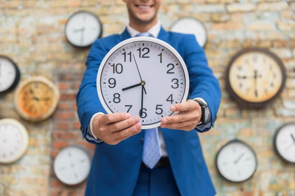 Hombre de traje de pie cerca de la pared con relojes — Foto de Stock