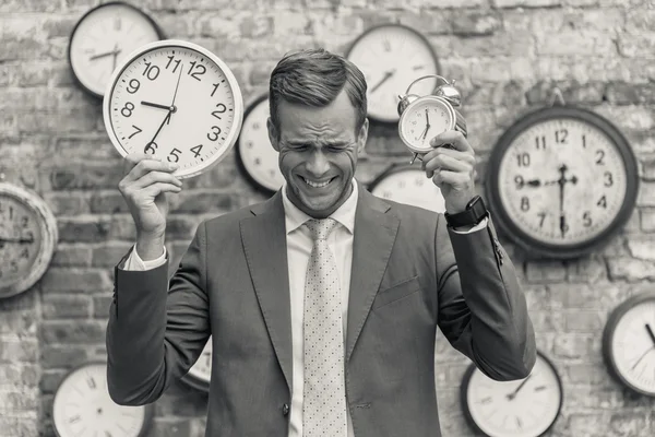 Hombre de traje de pie cerca de la pared con relojes — Foto de Stock