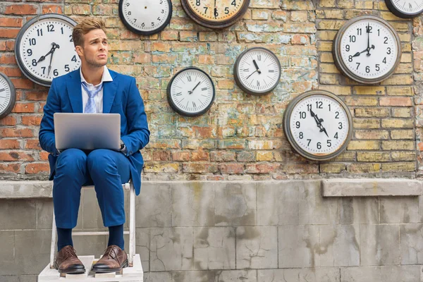 Homem de terno sentado perto da parede com relógios — Fotografia de Stock