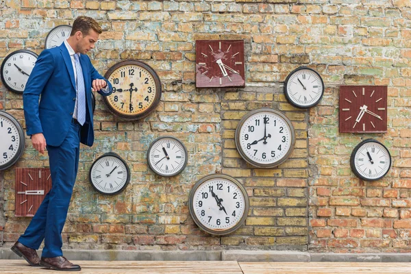 Man in suit standing near wall with clocks