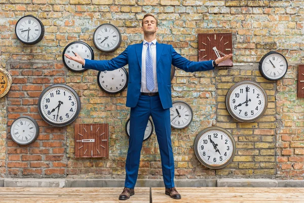 Hombre de traje de pie cerca de la pared con relojes — Foto de Stock