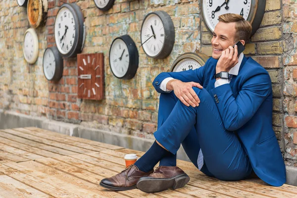 Hombre de traje sentado cerca de la pared con relojes — Foto de Stock