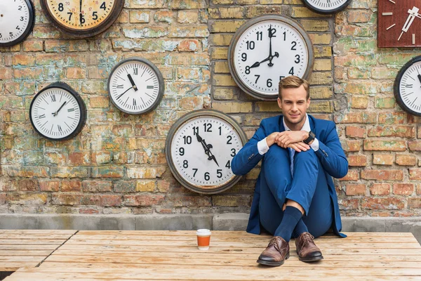 Hombre de traje sentado cerca de la pared con relojes — Foto de Stock