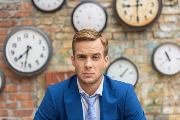 Hombre de traje sentado cerca de la pared con relojes — Foto de Stock