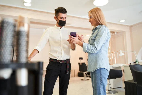 Žena ukazuje obrazovku smartphonu svému holiči — Stock fotografie