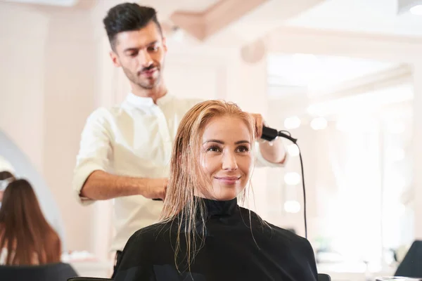 Stylist making hairstyle using hair dryer — Stock Photo, Image