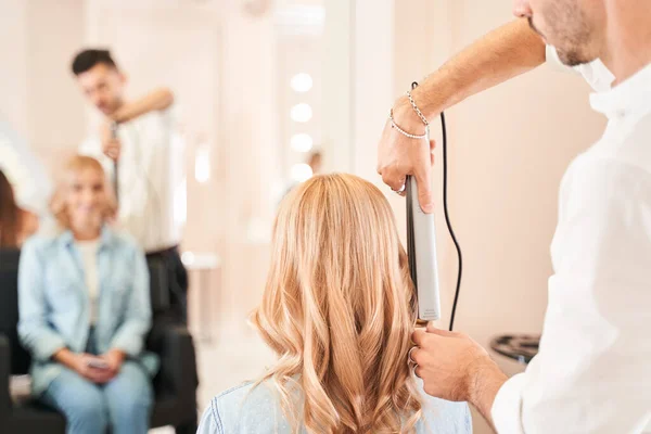 Парикмахер делает прическу с помощью щипцов для волос — стоковое фото