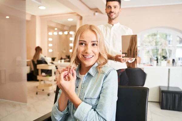 Mulher está olhando no espelho e tocando seu cabelo — Fotografia de Stock