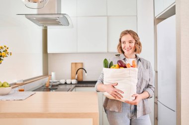 Ev hanımı, büyük bir poşet bakkala sarılıyor.