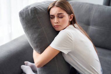 Kanepede oturan ve yastığını tutan kadın.