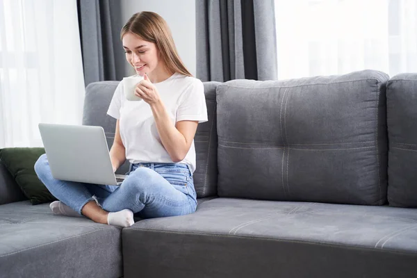 Kvinnan sitter i soffan med sin laptop — Stockfoto