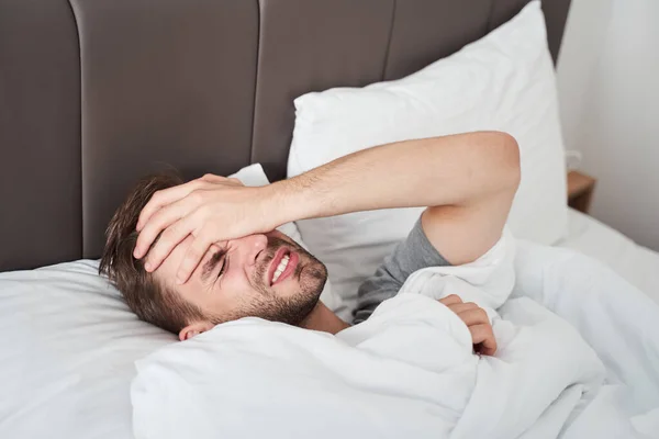 Man liggend op het bed en een sterk gevoel van hoofdpijn — Stockfoto