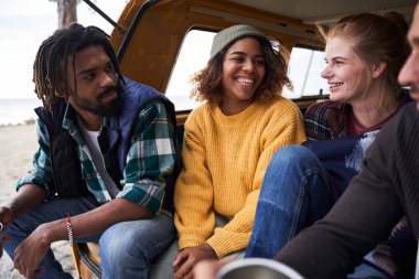 İnsanlar arabanın bagajında oturup konuşuyorlar.