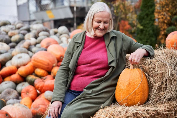 Woman sitting and relaxing at the haystack and looking at the big orange pumpkin — Stock Photo, Image