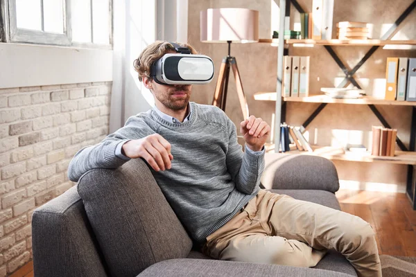 Mężczyzna siedzi w przytulnym salonie i za pomocą google VR — Zdjęcie stockowe