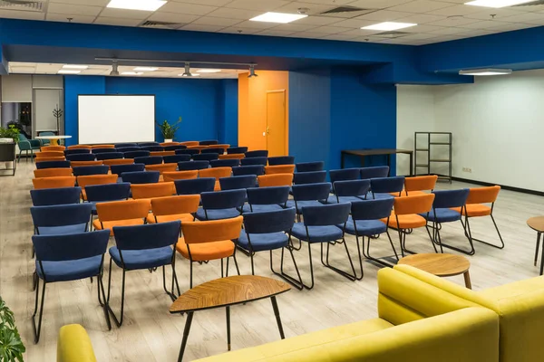 Sala de conferências com cadeiras laranja e azul e tela em branco — Fotografia de Stock