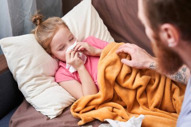 Baba hasta kızının yanında oturup burnunu siliyor.