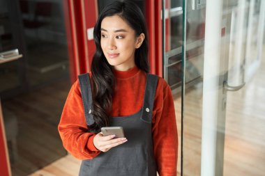 Gülümseyen siyah saçlı kadın elinde akıllı bir telefon tutuyor ve raporu için bilgi arıyor.