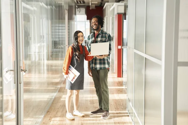 Sırıtma güdümlü öğrenci elinde dizüstü bilgisayarla grup arkadaşıyla sohbet ediyor.