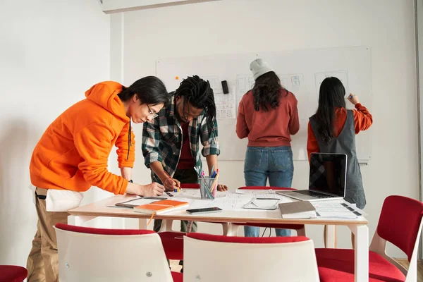 Dwóch studentów w stylowych ciuchach pracuje jako projektant aplikacji mobilnych z koleżankami z grupy — Zdjęcie stockowe