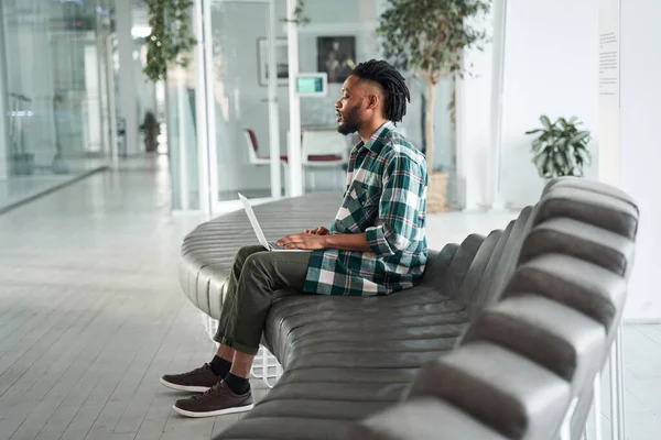 Portrait of a happy smart male student wearing plaid shirt using laptop