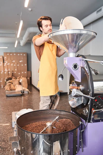 Çağdaş bir kızartma makinesine çiğ kahve çekirdeği döken adam. — Stok fotoğraf