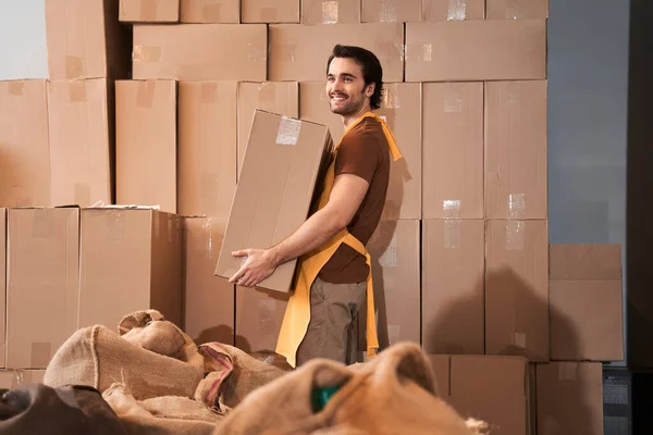 Worker wearing apron holding heavy box in hands — Stock Photo, Image