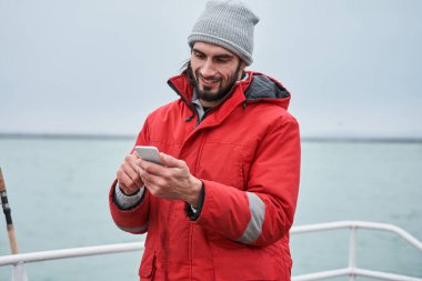 Balıkçı akıllı telefon ekranına bakıyor ve birine sesleniyor.