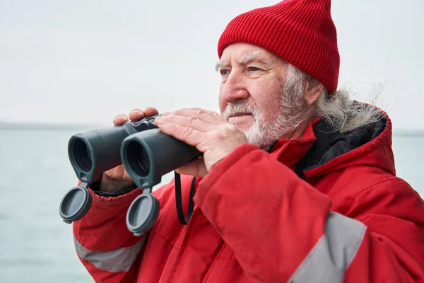 Fishing ship dressed in protective coat looking through binoculars — Stock Photo, Image