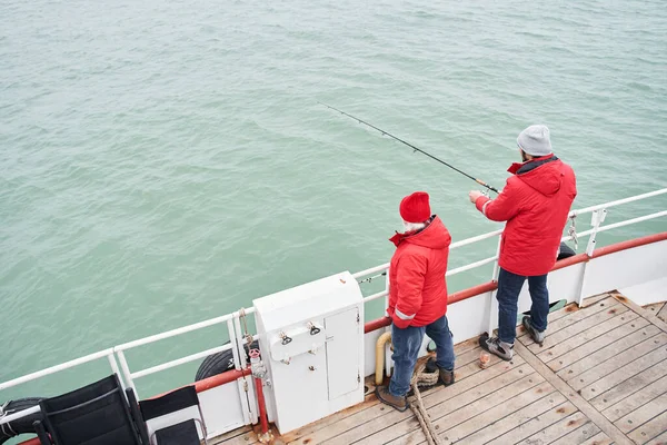 Моряк помогает усердному рыбаку вылавливать рыбу из моря — стоковое фото