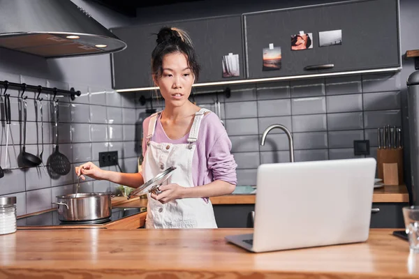 Жінка дивиться рецепт на свій ноутбук під час приготування їжі — стокове фото