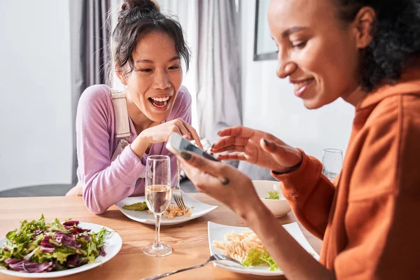 Девушки смеются, глядя на смартфон во время ужина — стоковое фото