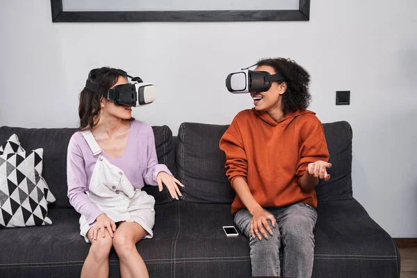 Las mejores amigas sentadas en el sofá y usando auriculares de realidad virtual — Foto de Stock