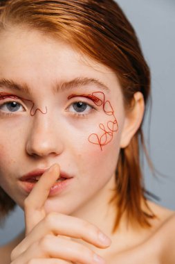 Yüzünde iplik olan bir kız sessizlik hareketi yapıyor.