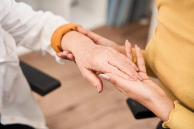 Kıdemli bir hastanın elini tutan ve dokunan bir tıp çalışanı.