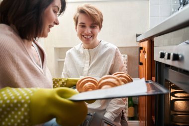 Bir kadın kız arkadaşıyla kruvasan hazırlıyor ve gülüyor.
