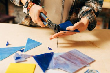 Kadın cımbızla, eritme ve işçilikle cam mozaiği yapıyor.