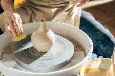 Adam çömlek çarkında seramik demlik yaparken temizlik için sünger kullanıyor.